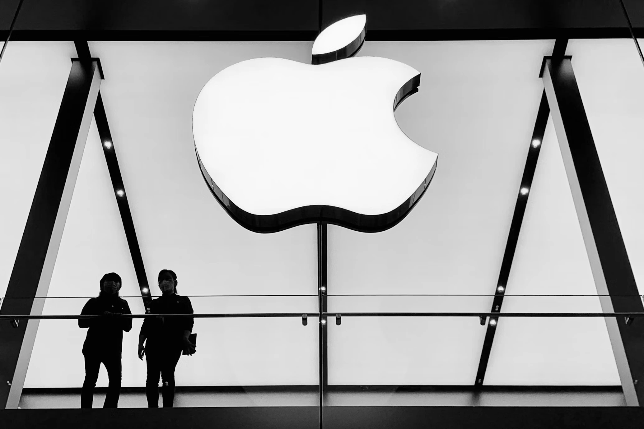 an apple logo on glass wall of a building outside and two people viewing this